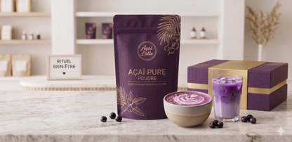 Pochette de poudre d'açai pure bio de la marque Açaï Latte, accompagnée d'un latte violet, d'un bol de smoothie et d'un coffret cadeau sur un comptoir en marbre